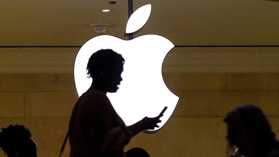 A women uses an iPhone mobile device as she passes a lighted Apple logo at the Apple store(Reuters)